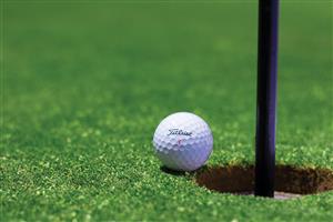 Golf ball sitting just on the edge of the hole with the flag inside.